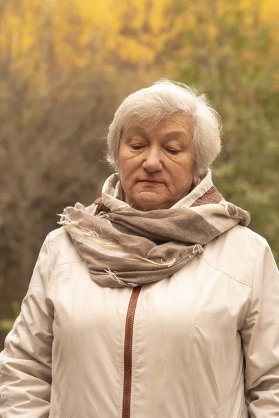 一位65岁的灰白头发妇女在秋天树木背景下的画像 — 图库照片