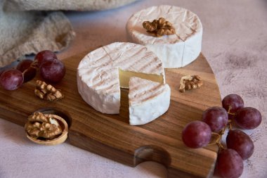 Beyaz küflü peynir, beyaz bir tezgahın üzerindeki tahta kesme tahtasındaki üzümler ve cevizler.
