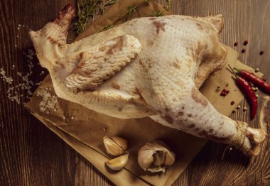 Taze çiğ et. Baharatları ve baharatları olan solgun bir tavuk leşi pişirmeye hazır, yemek kağıdının üzerinde yatıyor..