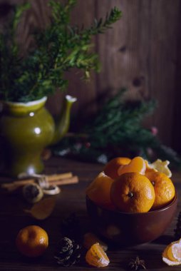Kahverengi bir seramik kasede taze taze mandalinalar yatıyor. Arka planda dallar.