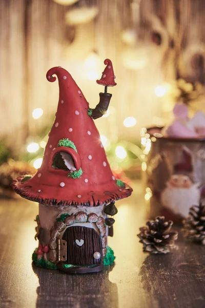 Parlak bir çelenk ve Noel dekorunun arka planında sinek şeklinde bir çatısı olan el yapımı kil ev..