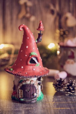 Parlak bir çelenk ve Noel dekorunun arka planında sinek şeklinde bir çatısı olan el yapımı kil ev..