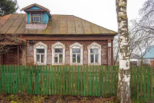 Uma velha casa de aldeia de madeira atrás de uma cerca . — Fotografia de Stock