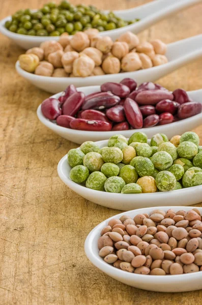 Various legumes on porcelain spoons — Stock Photo, Image