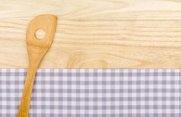 Wooden spoon on a purple checkered table cloth on a wooden background — Stock Photo, Image