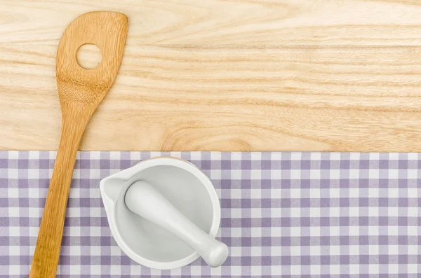 Wooden spoon and mortar on a purple checkered table cloth on a wooden background — Stock Photo, Image