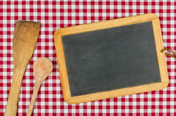 Pizarra vacía con cucharas de madera sobre un mantel a cuadros rojo — Foto de Stock