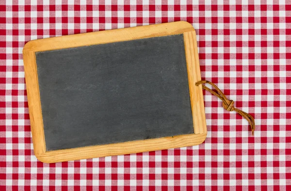 赤の市松模様のテーブル クロスにチョークで空の黒板 — ストック写真