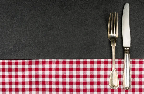 Silverware on a slate plate with a red checkered tablecloth — Stock Photo, Image