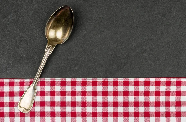 Cuchara de plata en un plato de pizarra con un mantel a cuadros rojo — Foto de Stock