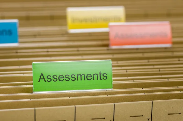 Hanging file folder labeled with Assessments — Stock Photo, Image