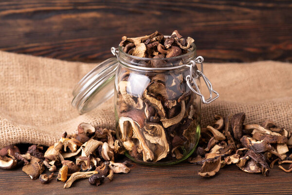 Dried aromatic wild forest mushrooms in a glass jar on wooden, rustic background 