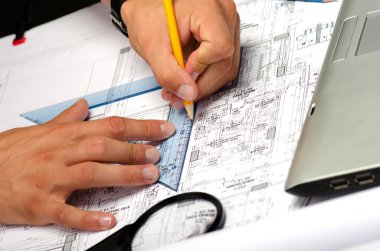 kalem ve bir büyüteç ile planları üzerinde çalışan adam