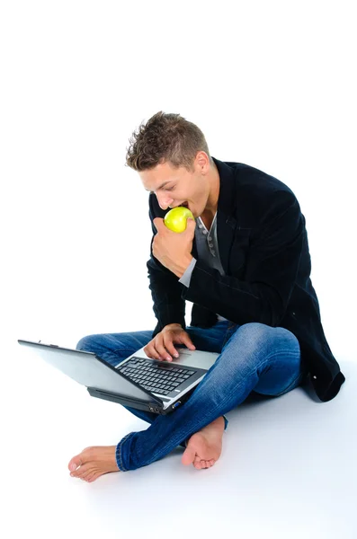 Jovem trabalhando no laptop e comendo maçã — Fotografia de Stock