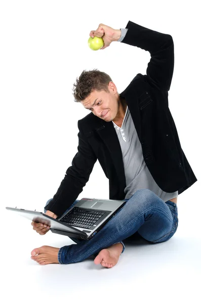 Angry young man working at laptop and eating apple — Stock Photo, Image