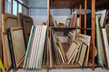 Resim, çerçeve ve sanat malzemeleriyle dolu ahşap raflar. Sanat galerisi deposu