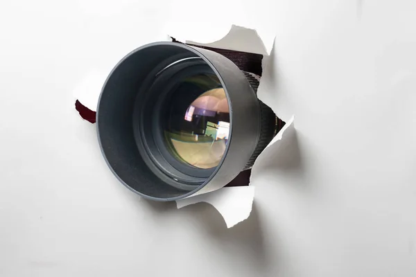 パパラッチや隠しカメラの概念は カメラのレンズは白い紙の壁に穴を通して外を見る — ストック写真