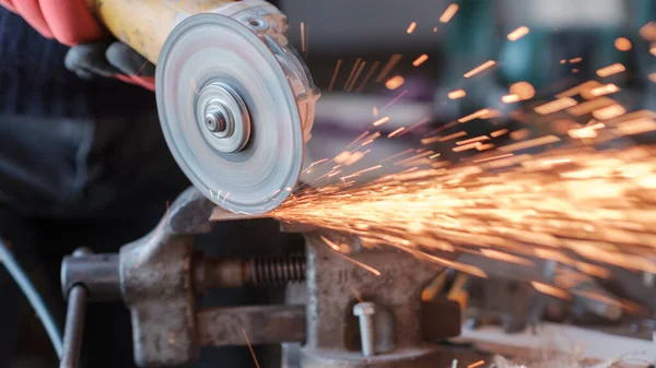 Üzerinde kıvılcımlar uçuşan bir metal üzerinde dairesel bir değirmenle çalışan işçiler, seçici bir odak noktası.