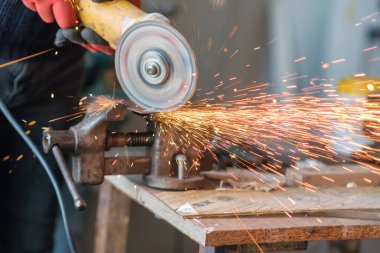 Üzerinde kıvılcımlar uçuşan bir metal üzerinde dairesel bir değirmenle çalışan işçiler, seçici bir odak noktası.