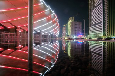 Su yüzeyine yansıyan modern mimari ile renkli ve aydınlık stadyum ve gece şehri manzarası