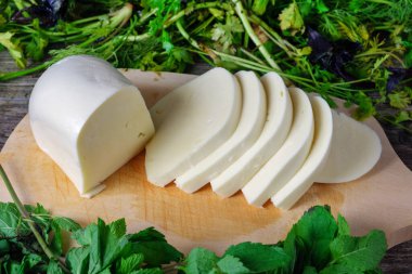 Gürcü peynirli sulguni. Ahşap bir tahtada dilimlenmiş peynir ve yeşil otlar.. 