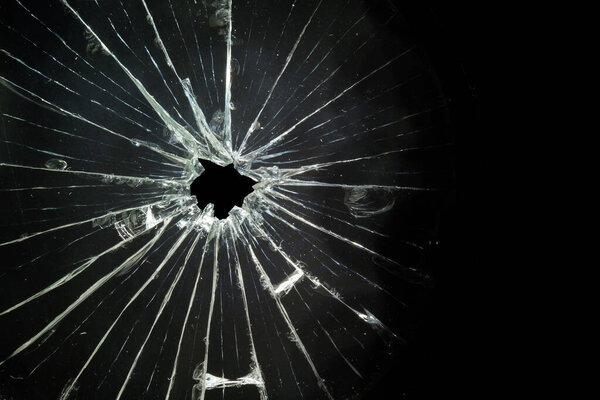 Дыра в разбитом и потрескавшемся стекле, крупным планом на тёмном фоне