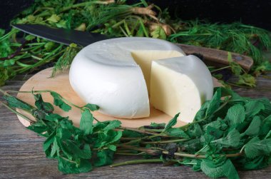Ahşap bir tahtanın üzerinde yeşil otlarla kaplı bir peynir. Gürcistan peyniri sulguni üst görünüm