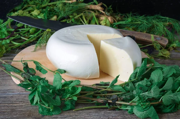 Ahşap bir tahtanın üzerinde yeşil otlarla kaplı bir peynir. Gürcistan peyniri sulguni üst görünüm