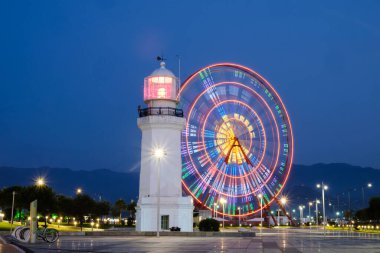 Gece aydınlık alanda dönme dolap ve deniz feneri.