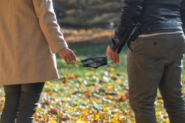 Kadın ve erkeğin arkasından yakından bakınca, soğuk ve güneşli bir sonbahar gününde, salgını durduran ya da birbirine bağlayan salgının sembolü olarak siyah tıp maskesi görülüyor.