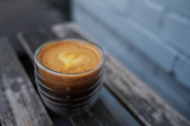 Bir fincan kahve tuğla bir duvara karşı ahşap bir masanın üzerinde duruyor. Portakal suyu ve espresso karışımına odaklan..