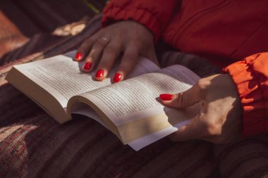 Kadınların elinde açık bir kitap. Parlak tırnaklı kız parkta kitap okuyor. Açık hava rahatlaması. Okuma hobisi. Güneşli bir günde kitap oku. Sonbahar tatili. Edebiyat ve eğitim kavramı. Huzurlu ve rahat bir dinlenme. Hikaye konsepti. Öğrenci.