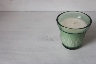 Beyaz ahşap rafta, yeşil cam vazoda mum. Beyaz arkaplanda yeni bir mum ve kop alanı. Aromaterapi konsepti. Kokulu mum izole edilmiş. İç mekan. Lüks bir yaşam tarzı. Şık ev dekorasyonu. 