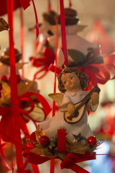Kırmızı kurdeleli Noel meleği. Panayırda Noel oyuncakları. Avrupa 'da şenlik pazarı. Noel dekorasyonu konsepti. Tatlı melek bebek. Noel alışverişi. Kış tatili konsepti. Yılbaşı arifesinin sihirli atmosferi. Aralık arka planı. 