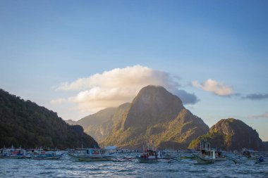 El Nido, Filipinler - 01 / 27 / 2020: Lagoon, El Nido 'da manzara gün batımı. Dağlı ve tekneli manzaralı bir akşam manzarası. Arka planda tekneleri ve adası olan tropik bir sahil. Alacakaranlıkta inanılmaz bir sahil. Tropikal turizm.