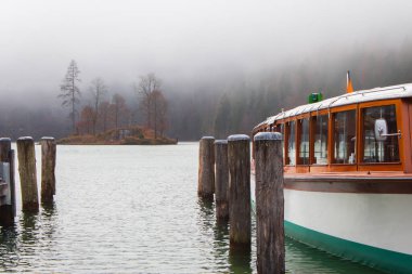 Fog on lake Kenigsee, Germany. Small island in the middle of the lake and tourist boat. Mist on lakeshore. German landscape. Autumn scenery in Europe, national Berchtesgaden park. Autumn nature.
