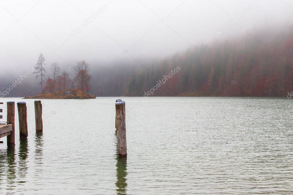 Fog on lake Kenigsee, Germany. Small island in the middle of the lake. Mist on lakeshore. German landscape. Autumn scenery in Europe, national Berchtesgaden park. Foggy day on lake. Autumn nature.
