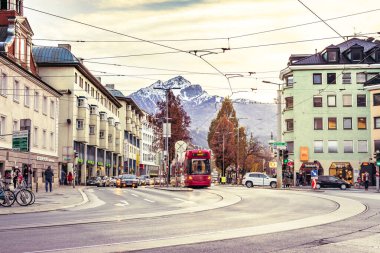 Innsbruck, Avusturya - 11.21.2021: Innsbruck sokaklarında yerel ulaşım ve turistler. Arkasında dağlar olan Innsbruck simgesi. Eski kasabanın merkezinde kırmızı tramvay ve arabalar.. 