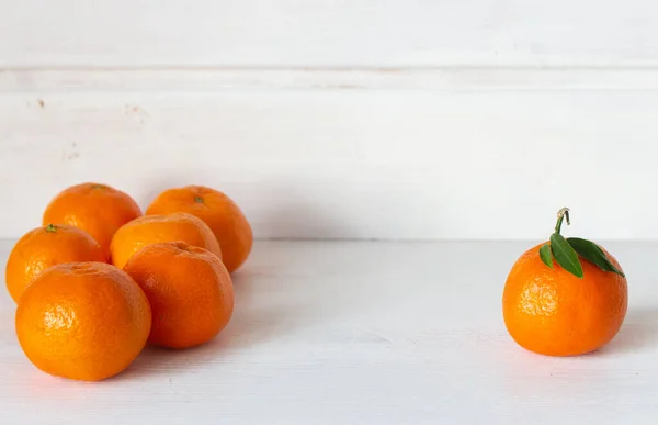 Tatlı narenciye meyveleri. Beyaz ahşap arka planda olgun mandalinalar. Tüm kavramlara karşı bir. Farklı bir konsept. Yapraklı bir mandalina ve yapraksız bir meyve grubu. C vitamini kavramı. 