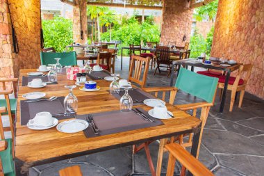 Tropikal tatil köyünde masa ayarı. Avluda masa hazır. Açık hava restoranının masasında çatal bıçak takımı. Lüks villadaki yemek masasında şarap kadehi ve bardak. Açık hava restoranı.