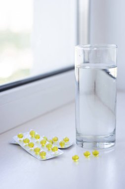 Sarı haplar ve beyaz arka planda bir bardak su. Sağlık hizmeti konsepti. Haplar ve kapsüller. İlaç ve eczane konsepti. Sarı haplar. Vitaminler kapsüllerde. Tıbbi tedavi. Haplar ve uyuşturucular.