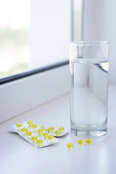 Yellow pills and glass of water on white background. Health care concept. Pills and capsules. Medicine and pharmacy concept. Yellow tablets. Vitamins in capsules. Medical treatment. Pills and drugs.