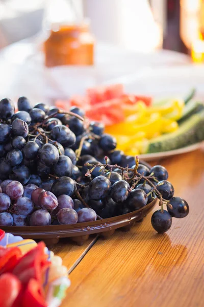Ripe grapes and fresh vegetables on background. Black grape on plate. Autumn harvest. Farming background. Vitamin in fruits and vegetables. Organic food. Healthy eating. Dinner table background.