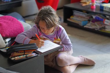 6-7 yaşlarındaki genç kız çiziyor, yazıyor.