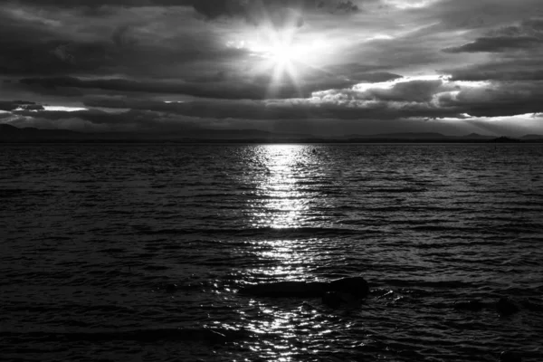 Tramonto sul lago Trasimeno in Umbria, con il sole che tramonta dietro nuvole lunatiche e bellissimi riflessi d'acqua — Foto Stock