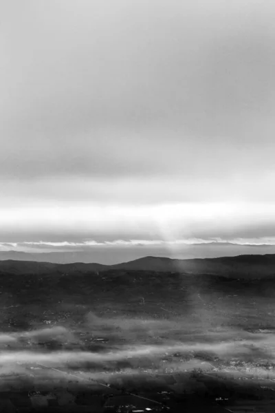 Rayons de soleil descendant de quelques nuages sur une vallée remplie de brouillard, éclairant une partie de celui-ci — Photo
