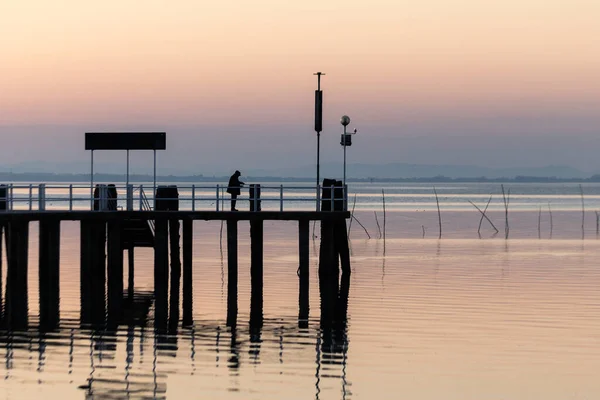 Man fishing on a pier on the lake at sunset — Stock Photo, Image