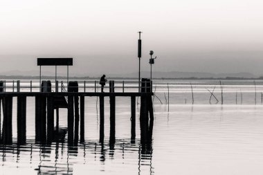 Man fishing on a pier on the lake at sunset.