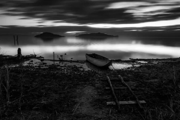 Long exposure view of shore of Trasimeno lake Umbria, Italy with a little boat at dusk, with perfectly still water and moving clouds.