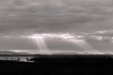 Gün batımına yakın güneş ışığı, arka planda kara bulutlar, Trasimeno Gölü üzerinde, Umbria, İtalya.